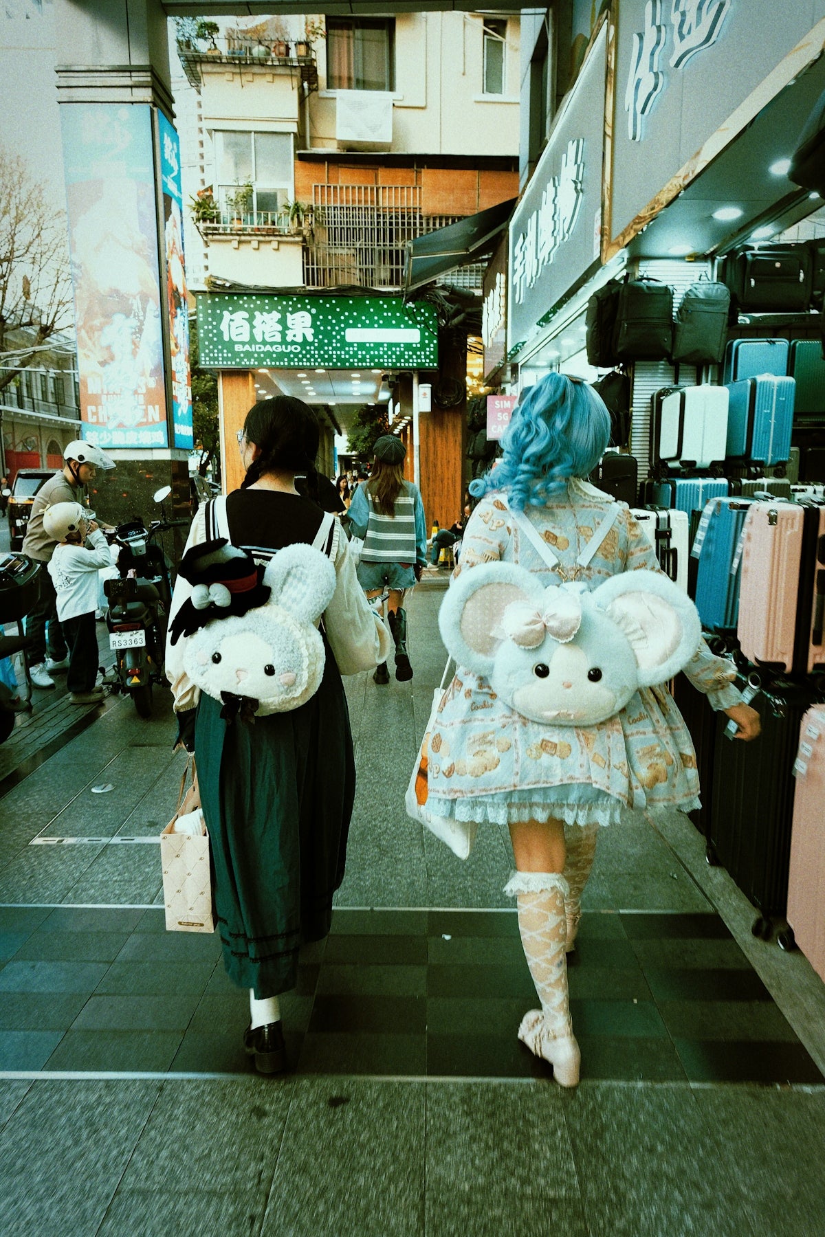 Two young women with plush backpacks walk down a street.