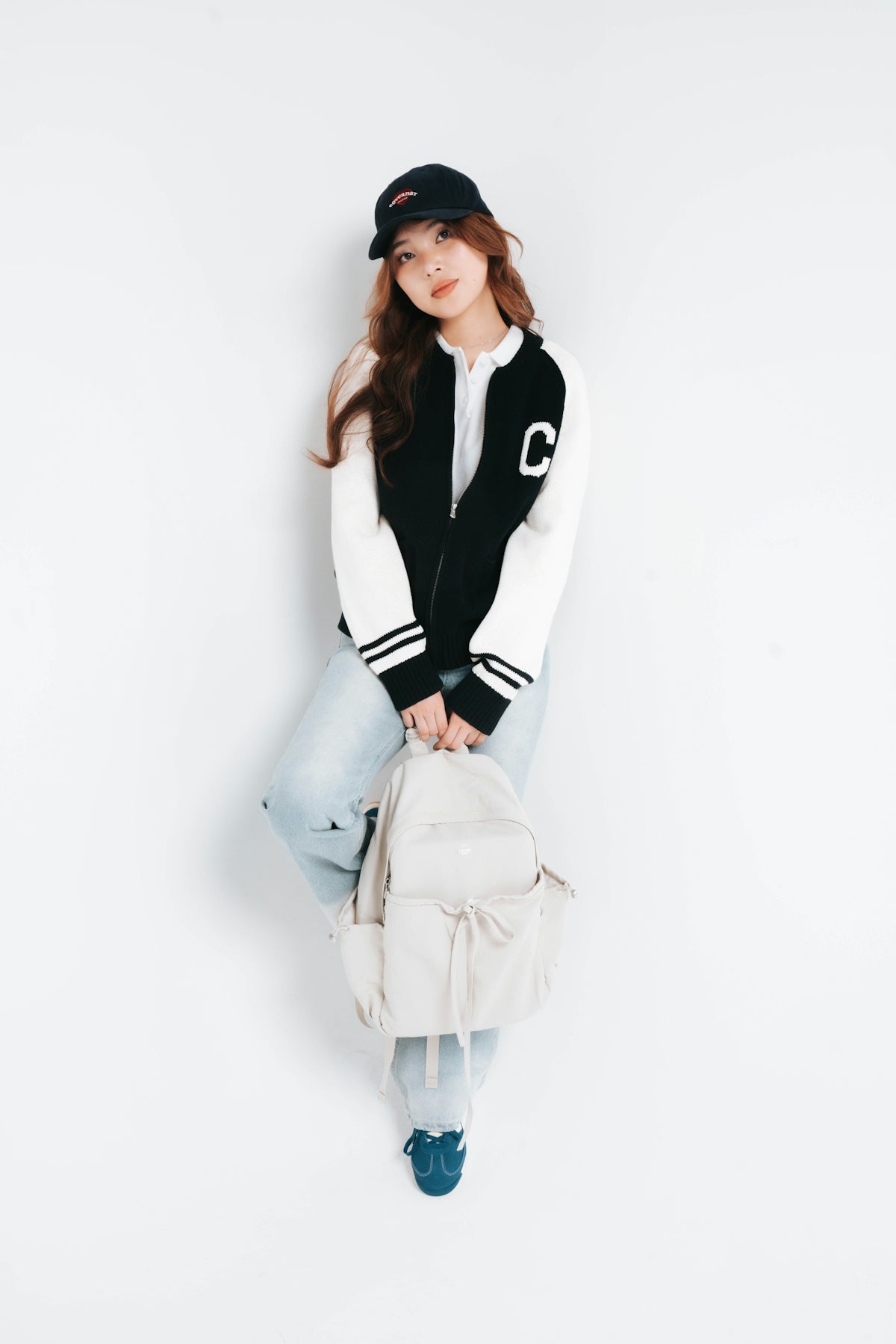 Young woman in baseball cap and bomber jacket with backpack.