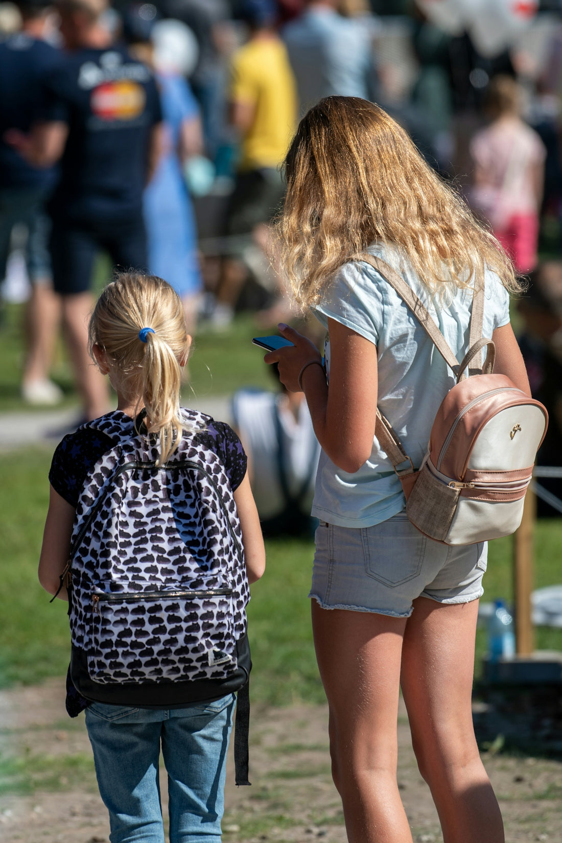 Two girls with backpacks in a crowd.