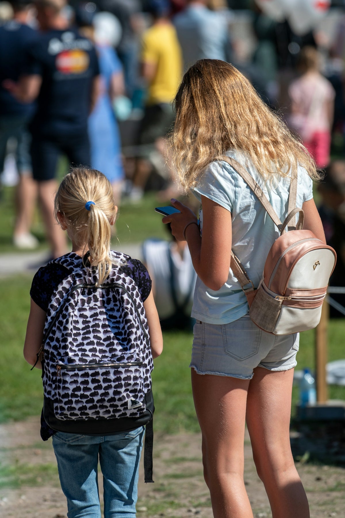 Two girls with backpacks in a crowd.