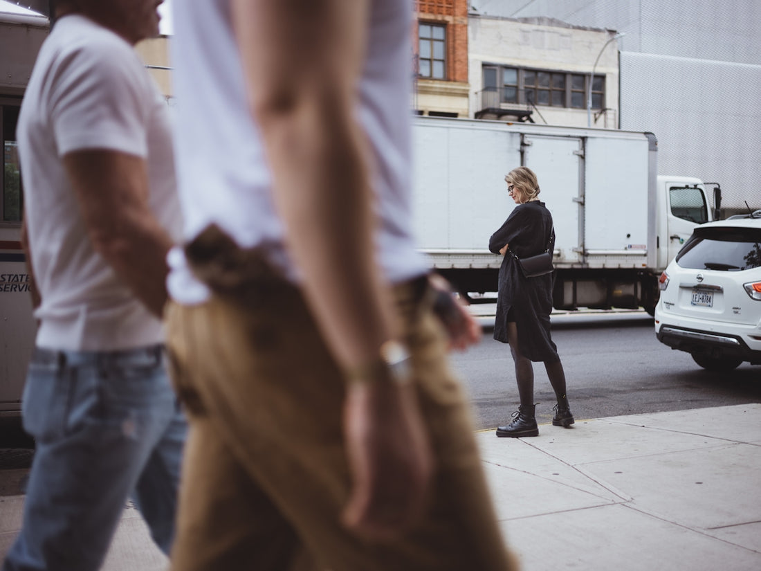 A woman in black stands on a city sidewalk.