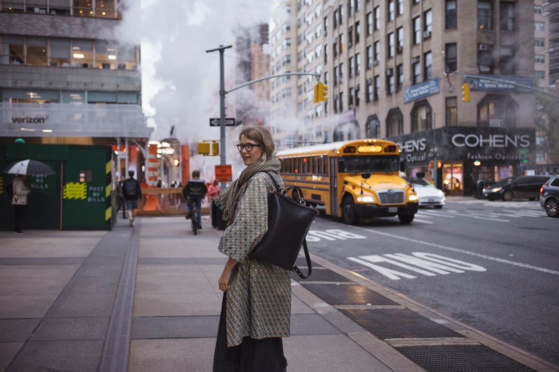 Woman on city sidewalk with yellow school bus passing.
