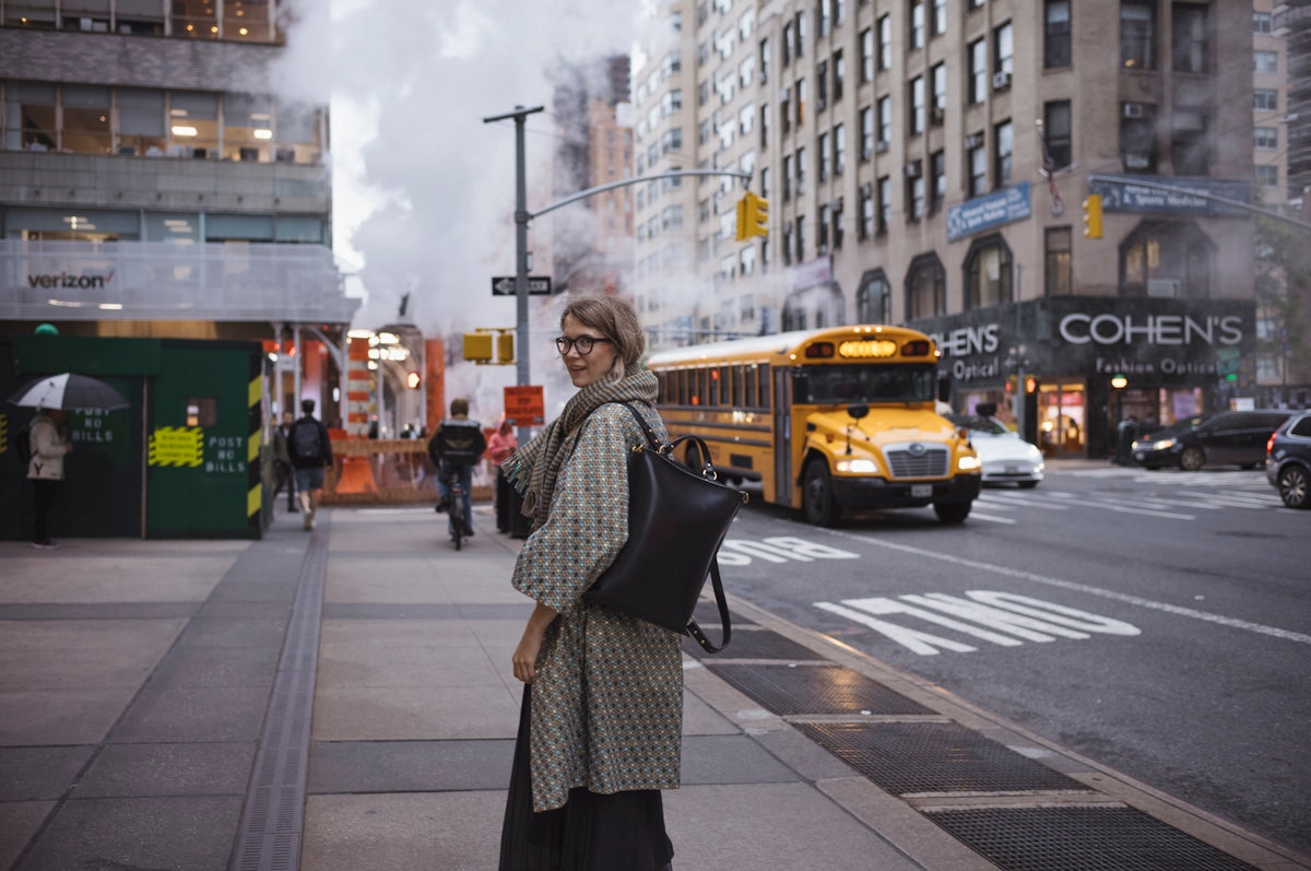 Woman on city sidewalk with yellow school bus passing.